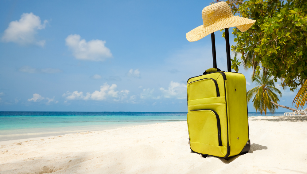 A yellow suitcase belonging to an eco-friendly tourist sits upright on a white sand beach.